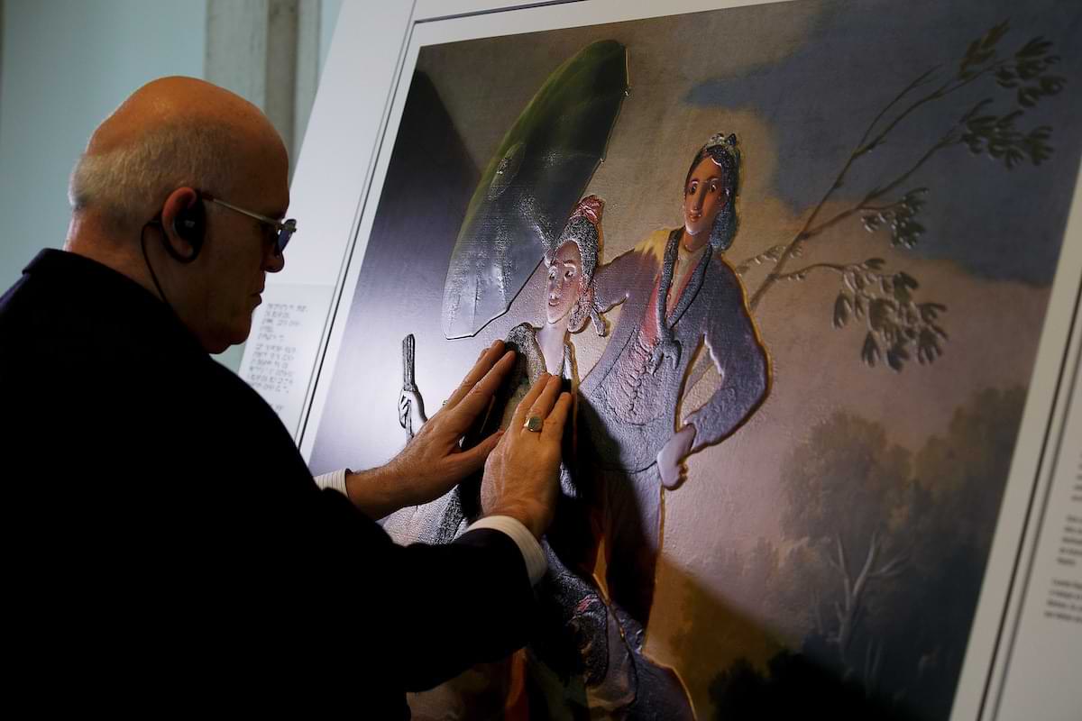 A visitor touches the raised 3D images of Goya’s The Parasol at the Hoy Toca el Prado exhibit (Come Touch the Prado) in Madrid, Spain. The 3D relief of a man and a
          woman with a parasol has raised the image enough to create depth and shape the visitor can physically feel