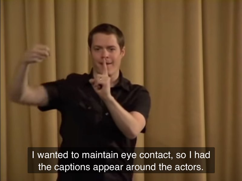 Betts signs and demonstrates how captions appear around an actor. Captions at the bottom read, "I wanted to maintain eye contact, so I had the captions appear around the actors."
