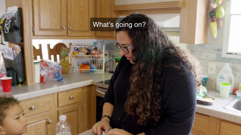 April Garcia is speaking to her son in their kitchen. Closed captions at the top of the screen read, "What's going on?"