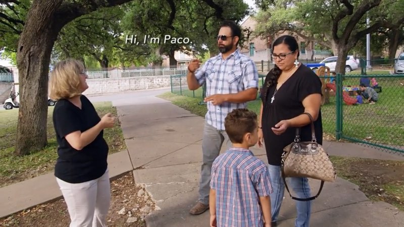 Paco, April, and their son Zade are on a school campus near a playground with another woman from the school. Paco signs to the woman as open subtitles appear near his head reading, "Hi, I'm Paco."