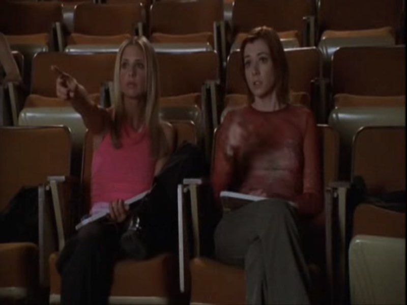 Buffy and Willow are seated in a classroom, pointing.