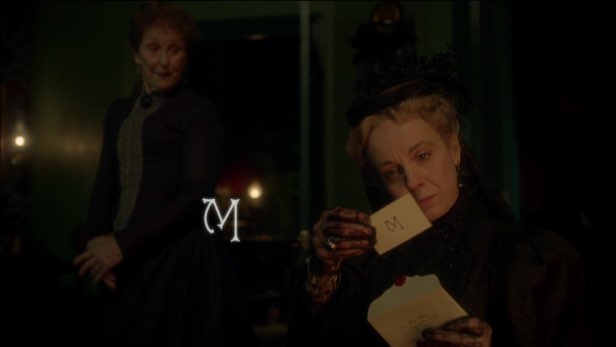 A woman in Victorian wear reads a handwritten note. The letter M is shown on the note in front of her and again as visual text next to her.