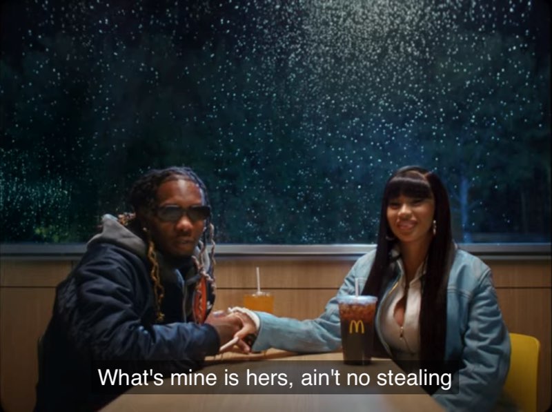 Rappers Offset and Cardi B are seated at a McDonald’s table, holding hands. Cardi B is smiling, both facing the camera. Closed captions at the bottom read, "What's mine is hers, ain't no stealing."