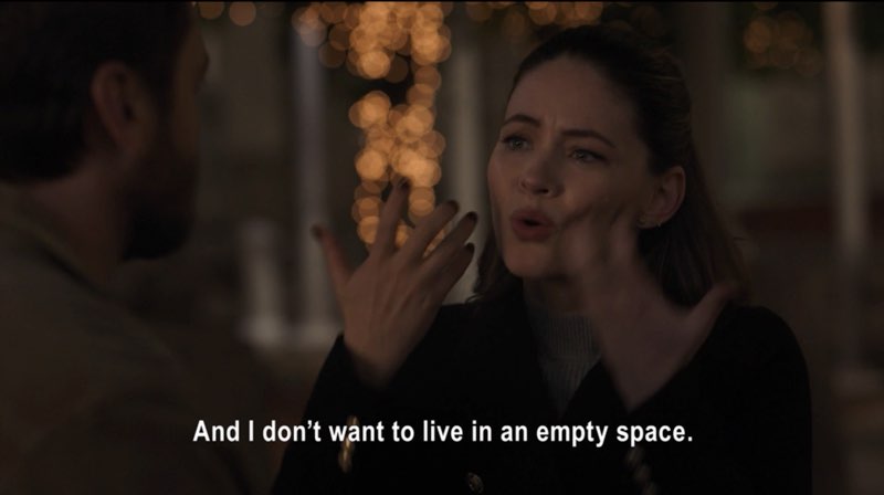 Max and Elizabeth, in regular clothes, are seated outside the hospital at night. Elizabeth is signing the words, don't want. Subtitles appear at the bottom of the screen that read, "And I don't want to live in an empty space."