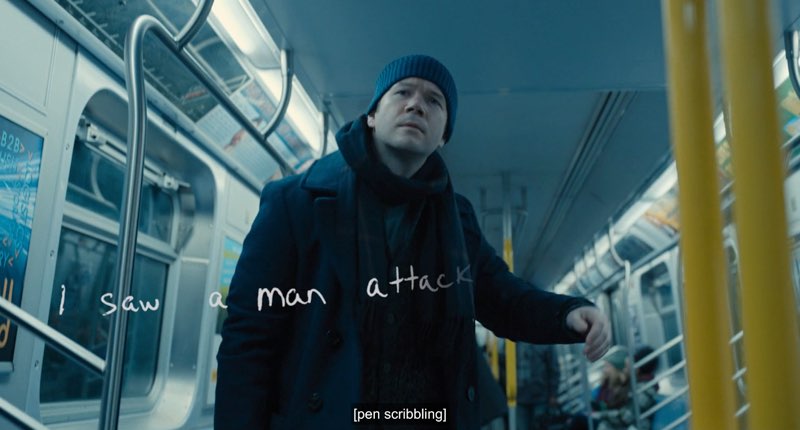 Theo stands up in a subway train and looks in front of him. Handwritten words are shown across the screen saying, "I saw a man." The rest of the phrase is being written out, showing "attack." Closed captions at the bottom of the screen read, "[pen scribbling]."