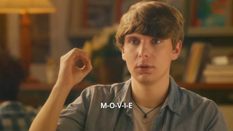 The male student in the library is signing the letter “o.” Subtitles at the bottom read, "M-O-V-I-E."