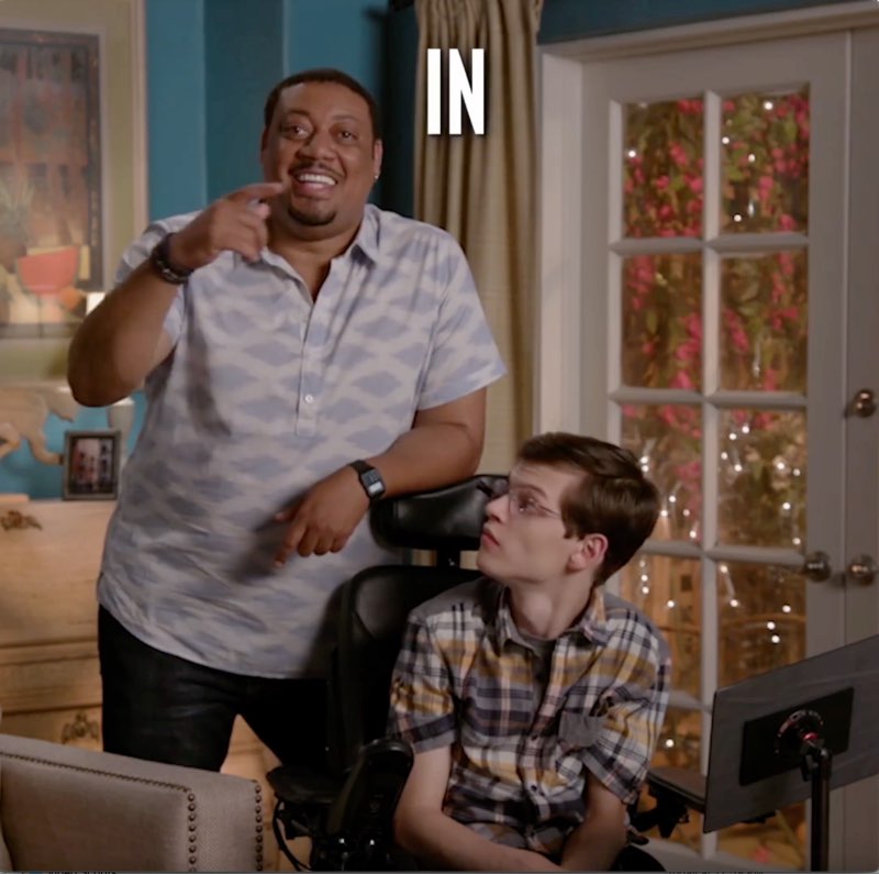 Cedric is standing next to Micah, speaking as he points to the area next to him where the word "In" appears.