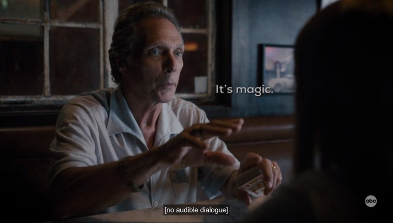 Leo is seated at a table in a bar and signing. Open subtitles appear next to him: "It's magic." Closed captions appear at the bottom and read, "[no audible dialogue]."