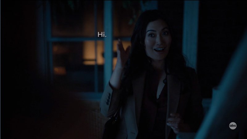 Emma is outside Charlie's place at night. She is signing, “Hi,” with a friendly open smile. Subtitles appear next to her that read, "Hi."