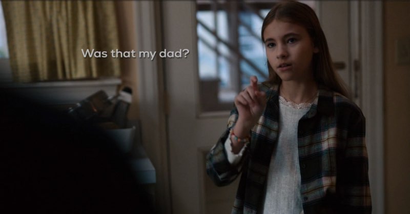 Ollie is in her kitchen signing, subtitles near her face. The subtitles read, "Was that my dad?"